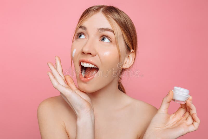 La fille choquée tient une crème hydratante dans sa main et l'applique à son visage pour hydrater la peau et pour enlever des rid photo libre de droits La fille choquée tient une crème hydratante dans sa main et l'applique à son visage pour hydrater la peau et pour enlever des rid photo libre de droits