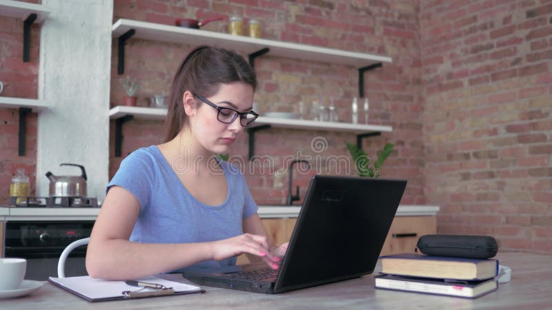 La fille d'indépendant dans des lunettes dactylographiant sur le clavier d'ordinateur portable et écrit des notes dans le press