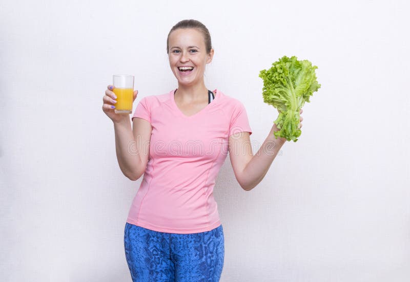 La fille dans des sports roses complètent tenir un verre de jus d'orange et d'un groupe de salade verte, les sourires de fille photos stock La fille dans des sports roses complètent tenir un verre de jus d'orange et d'un groupe de salade verte, les sourires de fille photos stock
