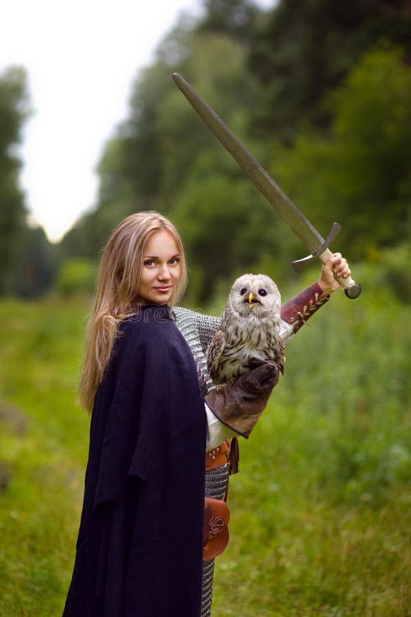 La fille dans l'armure avec le hibou tient une épée augmentée image stock La fille dans l'armure avec le hibou tient une épée augmentée image stock