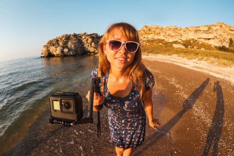 La fille dans la robe tire la vidéo sur la caméra d'action sur une plage sauvage image stock La fille dans la robe tire la vidéo sur la caméra d'action sur une plage sauvage image stock