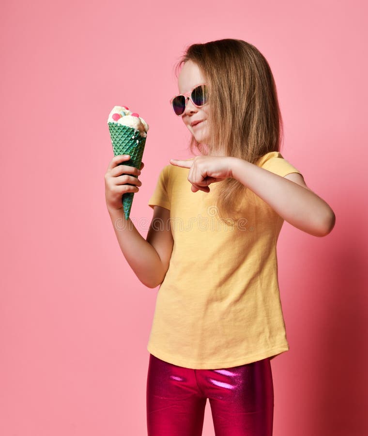 La fille de sourire astucieuse d'enfant dans le T-shirt et les-guêtres va à la grande glace à la vanille avec des bonbons dans le images stock