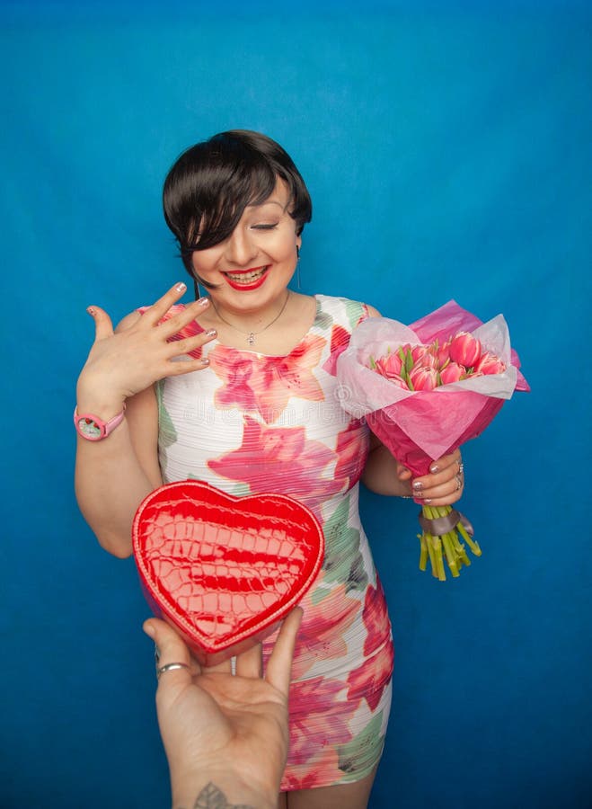 La fille de sourire mignonne dans une robe de ressort tient le bouquet frais rose des fleurs de tulipe sur un fond bleu dans le s photographie stock La fille de sourire mignonne dans une robe de ressort tient le bouquet frais rose des fleurs de tulipe sur un fond bleu dans le s photographie stock
