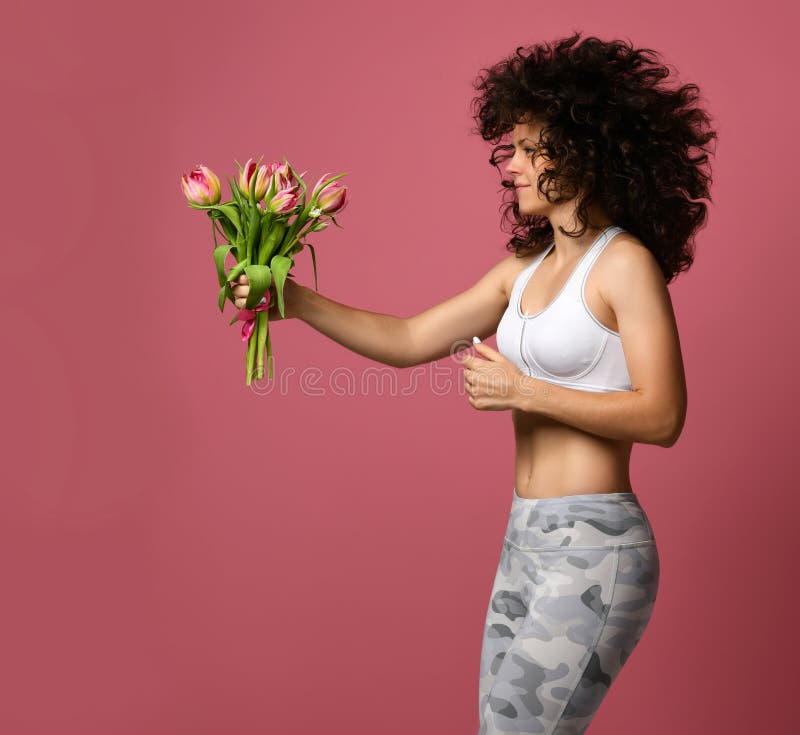 La fille de sports court sur un fond rose et porte un bouquet des tulipes dans sa main concept pour femme jour le 8 mars image libre de droits La fille de sports court sur un fond rose et porte un bouquet des tulipes dans sa main concept pour femme jour le 8 mars image libre de droits