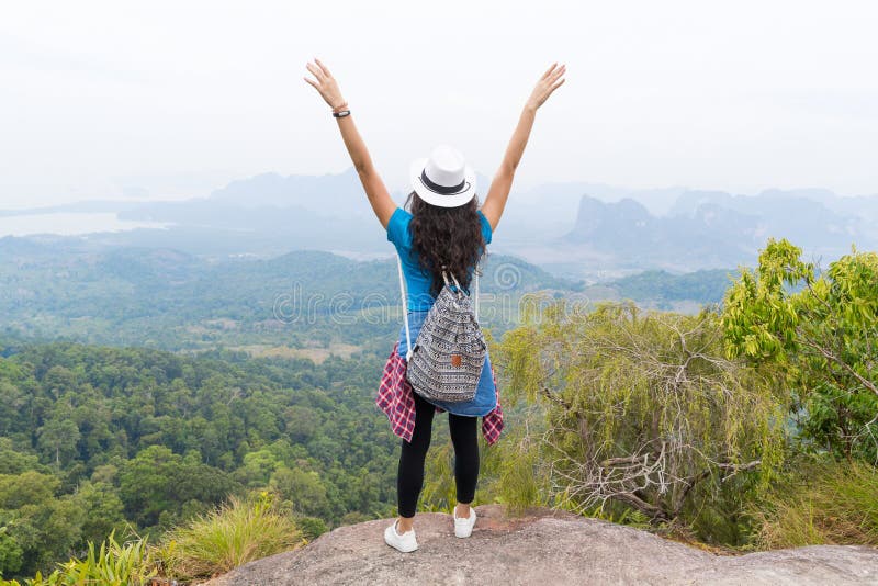 La fille de touristes avec le sac à dos se tenant sur de montagne de mains la vue arrière augmentée supérieure de retour apprécie image stock La fille de touristes avec le sac à dos se tenant sur de montagne de mains la vue arrière augmentée supérieure de retour apprécie image stock