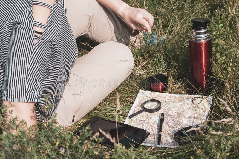 La fille de voyageur dans un T-shirt rayé et un pantalon brun s'assied sur l'herbe photos libres de droits La fille de voyageur dans un T-shirt rayé et un pantalon brun s'assied sur l'herbe photos libres de droits