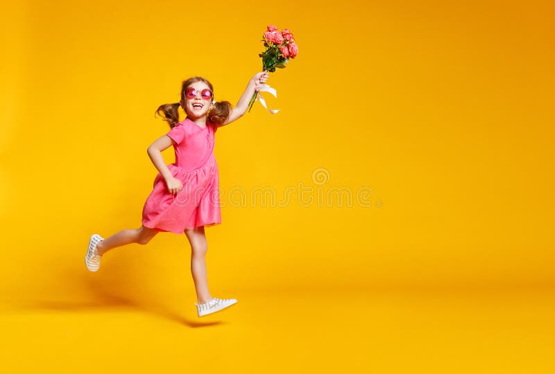 La fille drôle d'enfant court et saute avec le bouquet des fleurs sur la couleur images libres de droits La fille drôle d'enfant court et saute avec le bouquet des fleurs sur la couleur images libres de droits