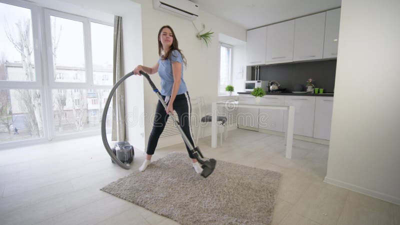 La fille drôle de femme de charge faisant des vides de nettoyage et ont la danse d'amusement et chantent dans la chambre à la mai