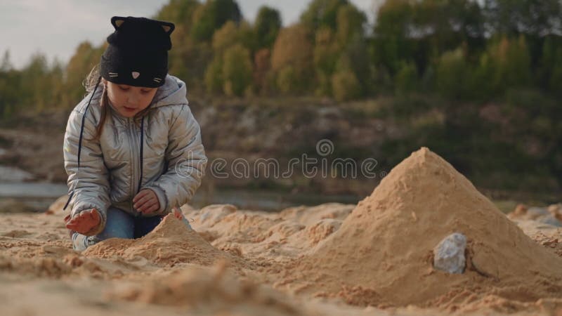 La fille est assis sur le littoral sablonneux et construit un château de sable