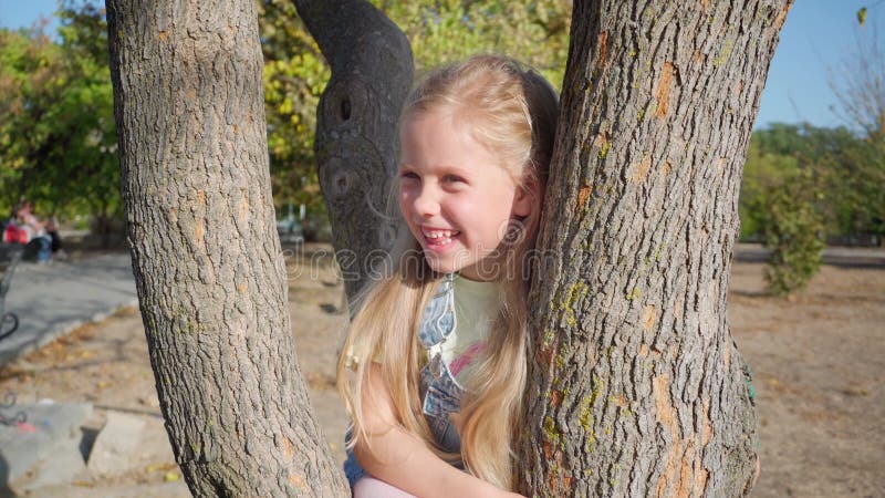 La fille est assise sur un arbre et sourit.