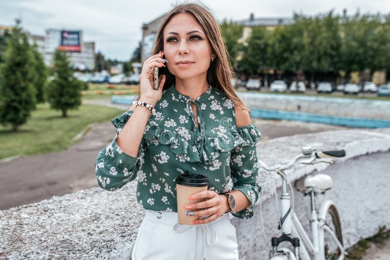 La fille fait appel au téléphone, pendant l'été dans la ville Arbres de vélo de fond Une tasse de th? de caf? Sourire de joie d'é photos stock La fille fait appel au téléphone, pendant l'été dans la ville Arbres de vélo de fond Une tasse de th? de caf? Sourire de joie d'é photos stock