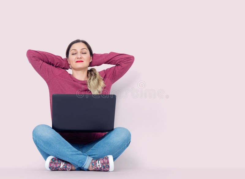 La fille heureuse avec les yeux fermés se reposant sur le plancher avec un ordinateur portable détendent dans la pose de lotus, s images stock La fille heureuse avec les yeux fermés se reposant sur le plancher avec un ordinateur portable détendent dans la pose de lotus, s images stock