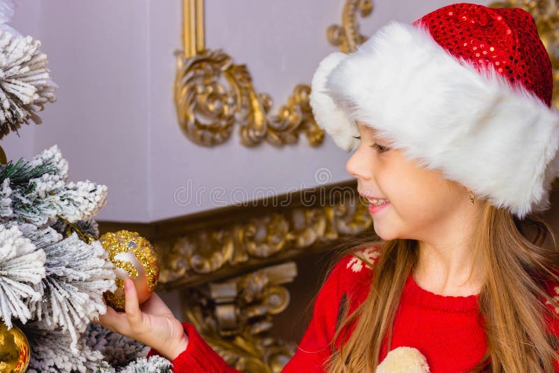 La fille heureuse mignonne dans le chapeau rouge accroche des décorations photo stock La fille heureuse mignonne dans le chapeau rouge accroche des décorations photo stock