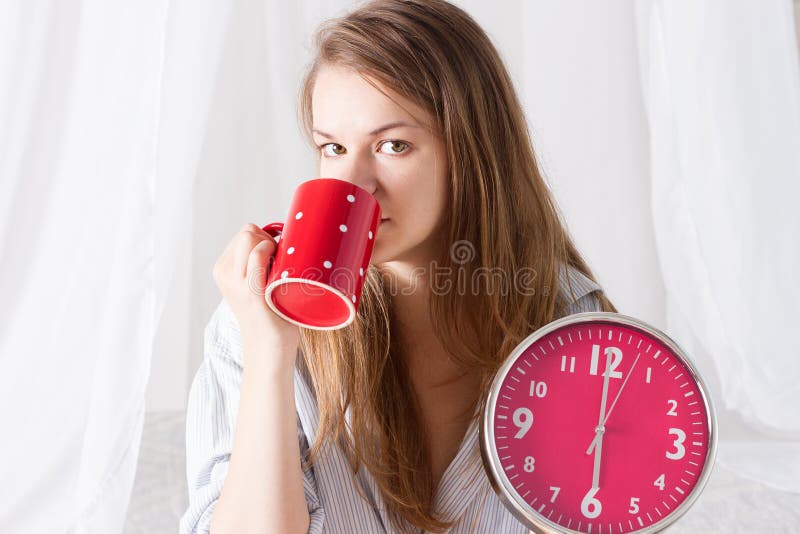 La fille heureuse se réveillent avec le réveil et le café photos stock La fille heureuse se réveillent avec le réveil et le café photos stock