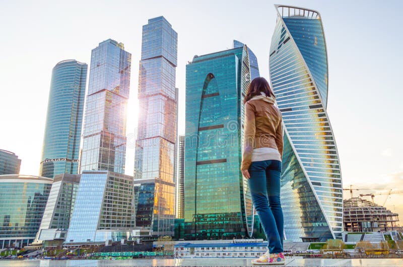 The girl looks at the sun and skyscrapers in the megalopolis. The girl looks at the sun and skyscrapers in the megalopolis.