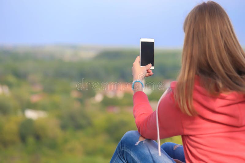 La fille s'asseyant sur un mur lui faisant face de retour et font la photo avec son smartphone