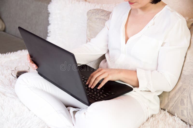 La fille s'assied à la maison sur le divan pour un ordinateur portable Travail ? la maison Femme d'affaires à la maison à l'ordin image stock La fille s'assied à la maison sur le divan pour un ordinateur portable Travail ? la maison Femme d'affaires à la maison à l'ordin image stock