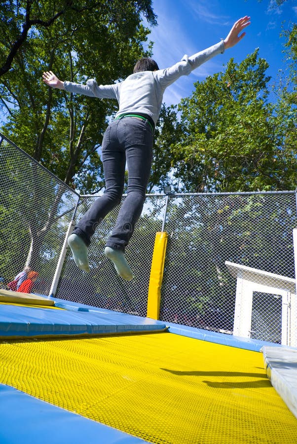 A girl bounces high, arms outstretched on a blue and yellow trampoline. A girl bounces high, arms outstretched on a blue and yellow trampoline.