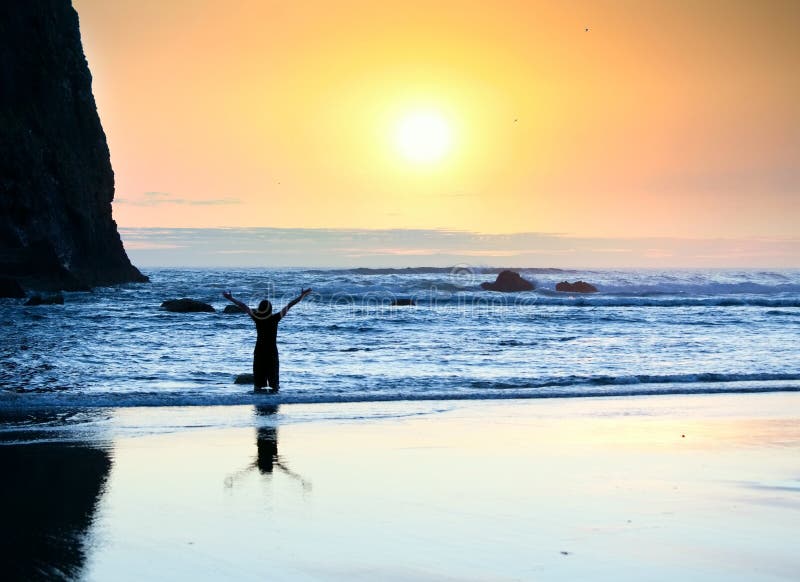 Silhouette of girl standing in waves, arms raised in praise to God at sunset. Silhouette of girl standing in waves, arms raised in praise to God at sunset