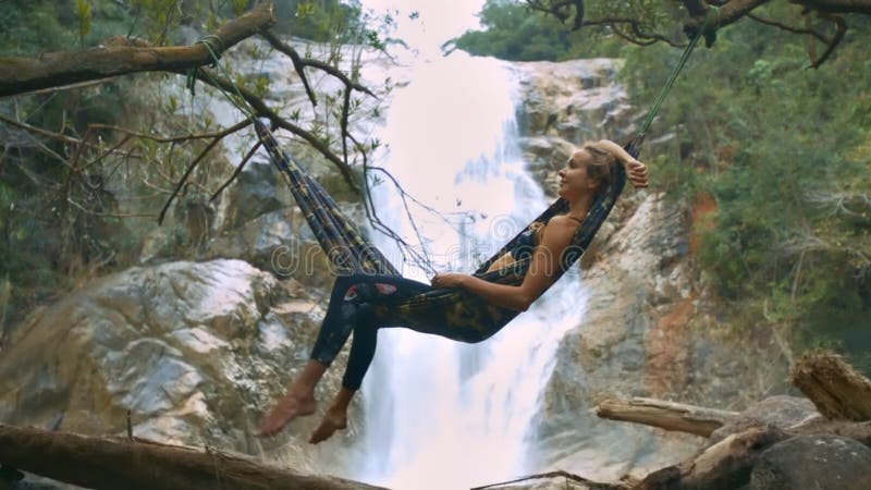 La fille se trouve sur l'hamac contre la cascade imagée