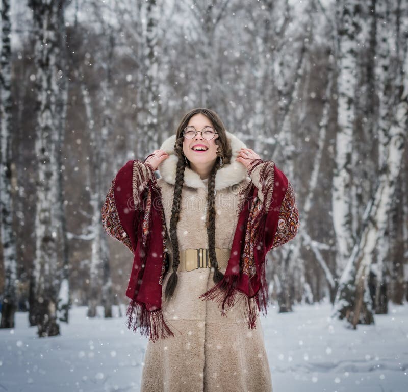 La fille sourit dans le jour d'hiver froid dehors en parc neigeux parmi des arbres