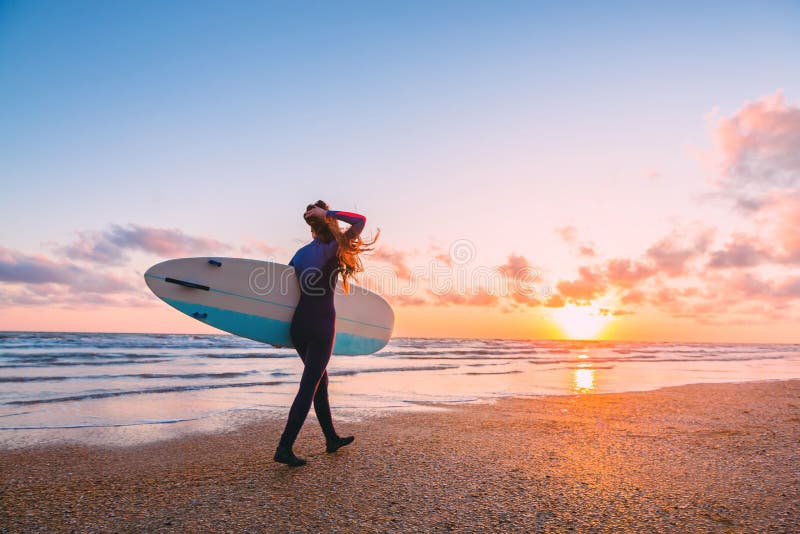 La fille sportive de ressac vont à surfer Femme avec la planche de surf et le coucher du soleil ou le lever de soleil sur l'océan images libres de droits La fille sportive de ressac vont à surfer Femme avec la planche de surf et le coucher du soleil ou le lever de soleil sur l'océan images libres de droits