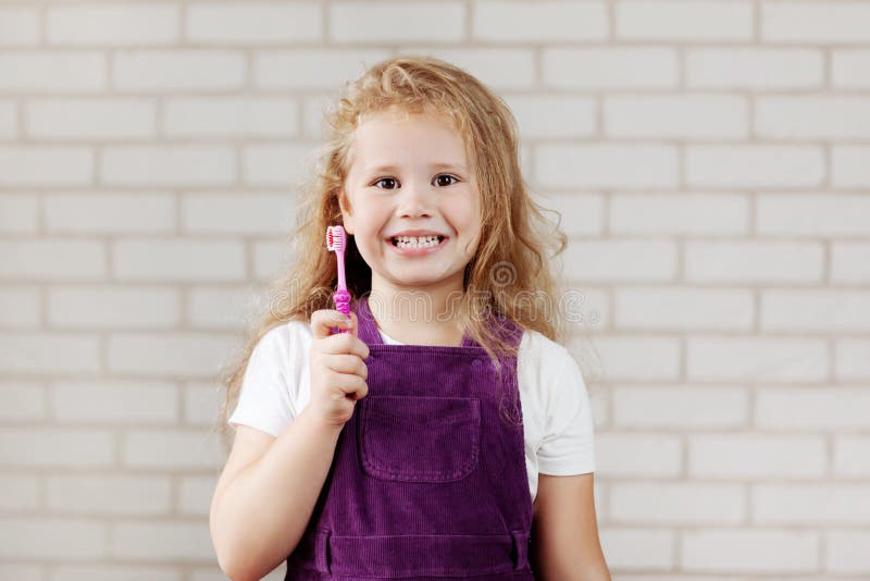 The girl is holding a bright pink toothbrush. Oral care, hygiene, prevention. The girl is holding a bright pink toothbrush. Oral care, hygiene, prevention.