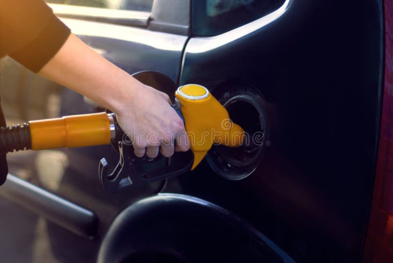 La fille à la station service avec un tuyau dans sa main et suffisances la voiture avec l'essence photographie stock libre de droits La fille à la station service avec un tuyau dans sa main et suffisances la voiture avec l'essence photographie stock libre de droits