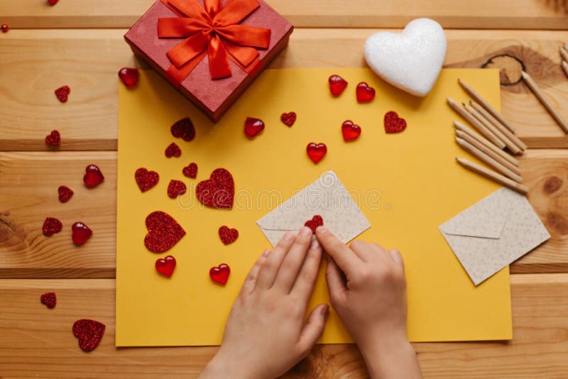 The girl wrote a letter with congratulations and pastes the envelope with a symbol in the form of a heart. Nearby lie various objects symbolizing the event. Creative space. The girl wrote a letter with congratulations and pastes the envelope with a symbol in the form of a heart. Nearby lie various objects symbolizing the event. Creative space.