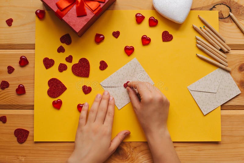 The girl wrote a letter with congratulations and pastes the envelope with a symbol in the form of a heart. Nearby lie various objects symbolizing the event. Creative space. The girl wrote a letter with congratulations and pastes the envelope with a symbol in the form of a heart. Nearby lie various objects symbolizing the event. Creative space.