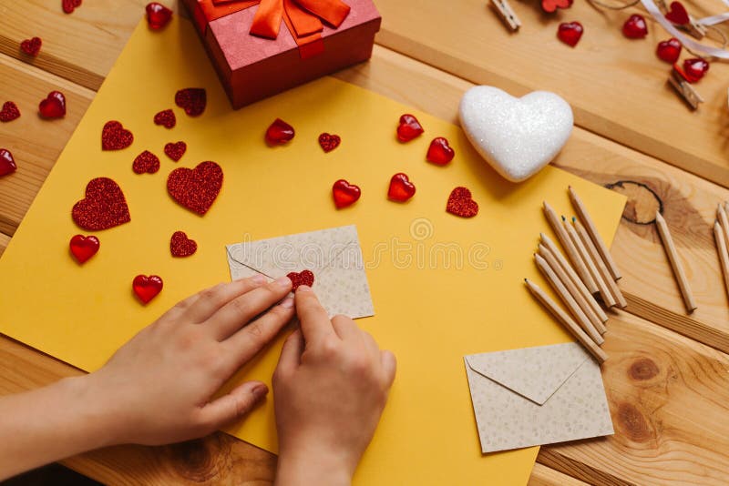 The girl wrote a letter with congratulations and pastes the envelope with a symbol in the form of a heart. Nearby lie various objects symbolizing the event. Creative space. The girl wrote a letter with congratulations and pastes the envelope with a symbol in the form of a heart. Nearby lie various objects symbolizing the event. Creative space.