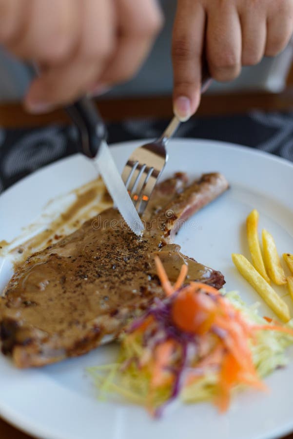 La fin vers le haut de la sauce au poivre noire à bifteck de côtelette de porc, les légumes et les pommes frites avec les hommes photographie stock libre de droits La fin vers le haut de la sauce au poivre noire à bifteck de côtelette de porc, les légumes et les pommes frites avec les hommes photographie stock libre de droits