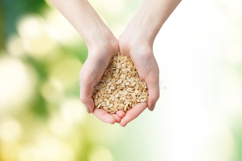 Healthy eating, dieting, vegetarian food and people concept - close up of woman hands holding oatmeal flakes over green natural background. Healthy eating, dieting, vegetarian food and people concept - close up of woman hands holding oatmeal flakes over green natural background