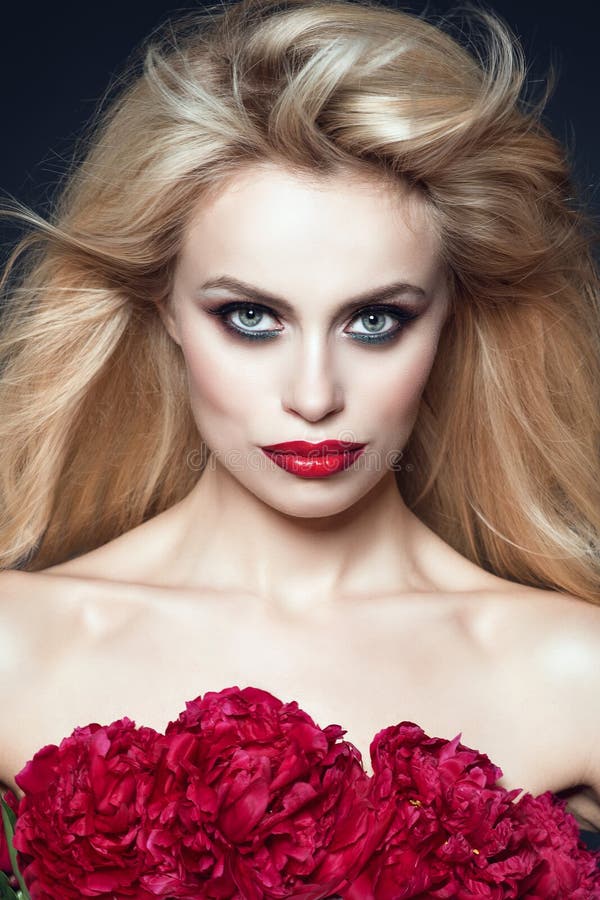 La fine sul ritratto di bello modello con capelli biondi che soffiano nel vento e perfetti compone Mazzo di peonie che coprono il fotografia stock La fine sul ritratto di bello modello con capelli biondi che soffiano nel vento e perfetti compone Mazzo di peonie che coprono il fotografia stock