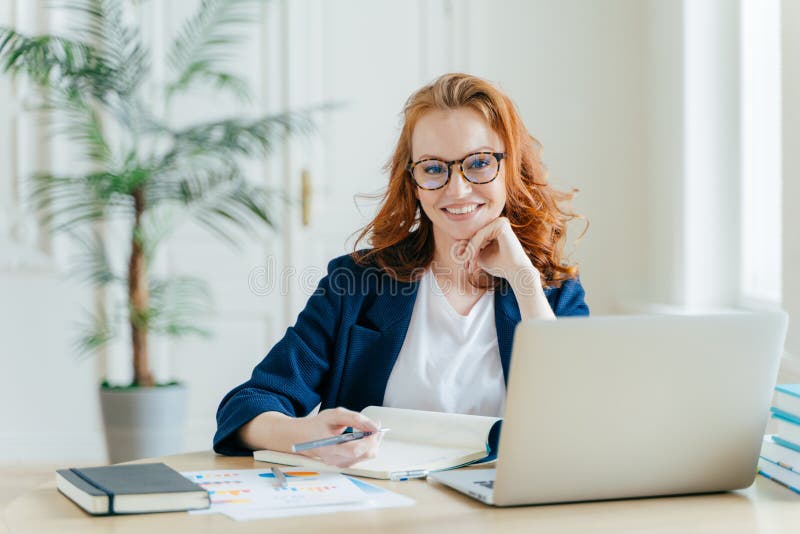 La foto delle free lance femminili del riuscito zenzero ha lavoro a distanza, guarda online webinar sul computer portatile, annot fotografia stock