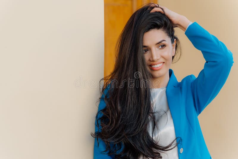 La foto di bella donna castana splendida tiene la mano sulla testa, ha capelli scuri lunghi si è pettinata da un lato, vestito in immagini stock libere da diritti La foto di bella donna castana splendida tiene la mano sulla testa, ha capelli scuri lunghi si è pettinata da un lato, vestito in immagini stock libere da diritti