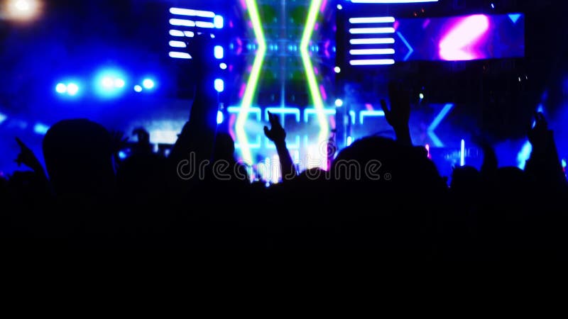 La foule au premier rang fait la fête. silhouettes de ventilateurs lever la main devant les lumières vives colorées strobing sur s