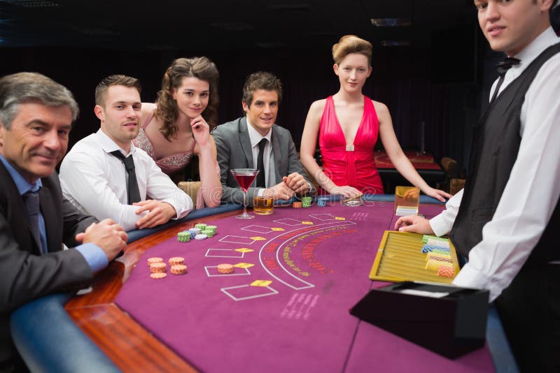 La gente che si siede al black jack presenta sorridere al casinò fotografia stock La gente che si siede al black jack presenta sorridere al casinò fotografia stock