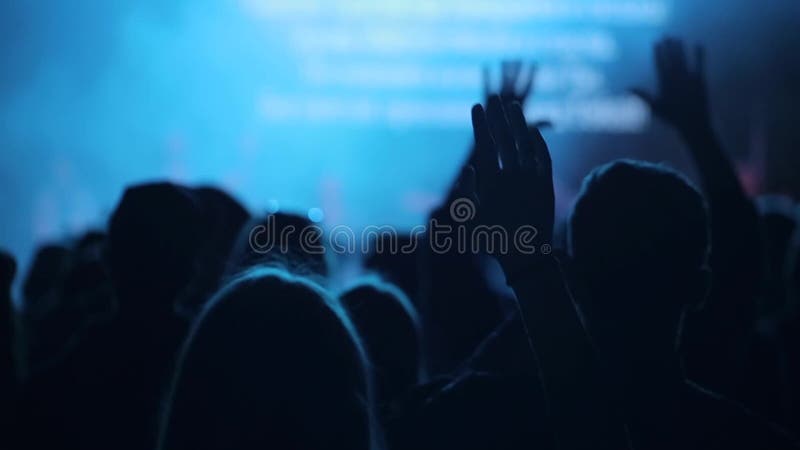La gente che solleva sulle mani ad un concerto r Una vista posteriore canto Fase vaga