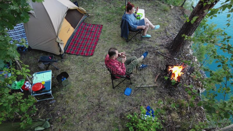 La gente disfruta acampando con carpas cerca de una fogata con vistas a un lago turquesa