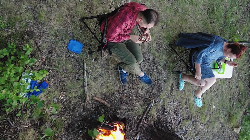 La gente disfruta acampando con carpas cerca de una fogata con vistas a un lago turquesa. vídeo vertical