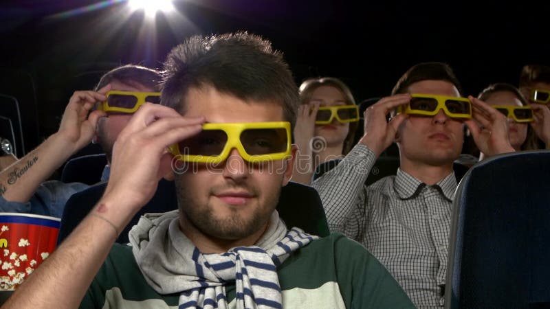 La gente joven lleva los vidrios 3D para mirar una película en