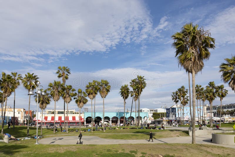 La gente si gode una passeggiata panoramica sulla spiaggia con palme e case colorate a Venice Beach in California fotografia stock La gente si gode una passeggiata panoramica sulla spiaggia con palme e case colorate a Venice Beach in California fotografia stock
