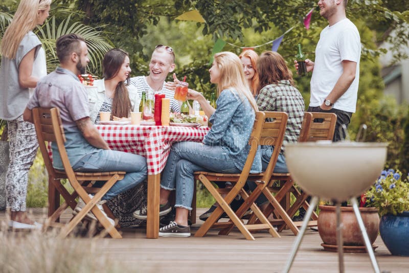 La gente si è riunita intorno ad una tavola di legno, al cibo, bere e al havi immagini stock La gente si è riunita intorno ad una tavola di legno, al cibo, bere e al havi immagini stock