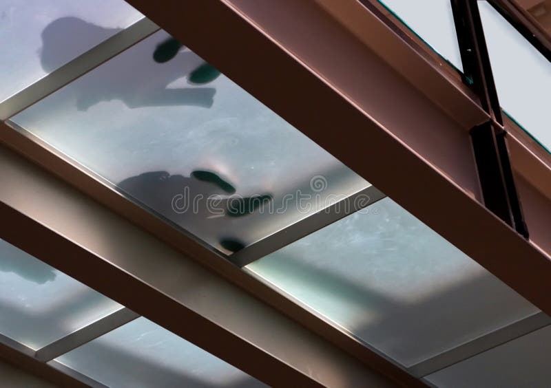 Silhouette of elevator waiting customers feet as seen through strong heat laminated glass flooring. Silhouette of elevator waiting customers feet as seen through strong heat laminated glass flooring