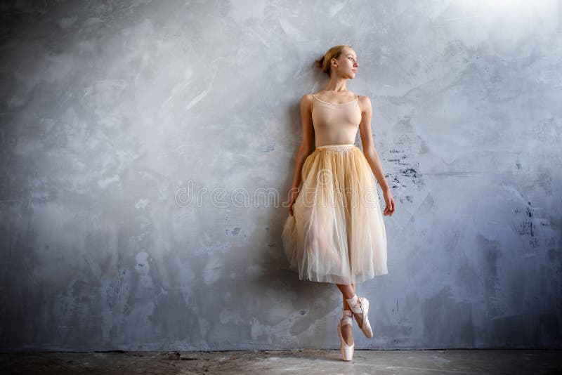 La giovane ballerina in un costume ballante colorato dorato sta posando in uno studio del sottotetto
