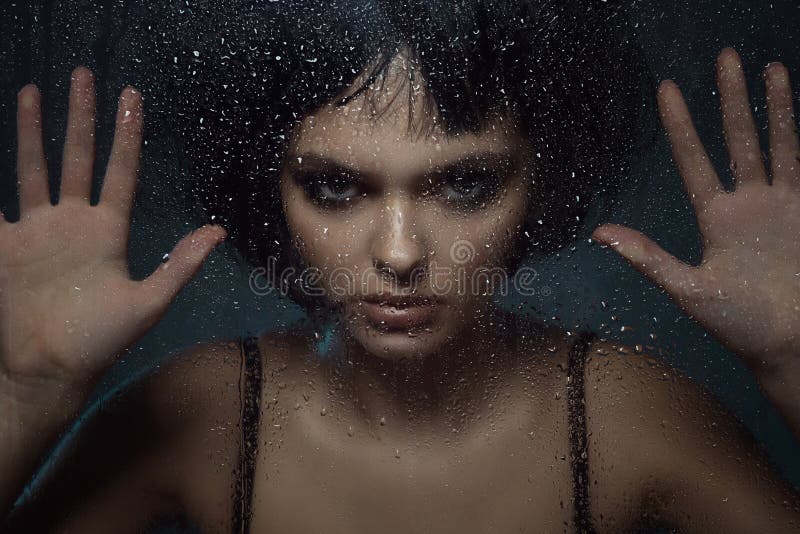 La giovane bella donna con provocatorio compone e condizione alla moda di taglio di capelli del peso dietro la finestra con le go immagine stock La giovane bella donna con provocatorio compone e condizione alla moda di taglio di capelli del peso dietro la finestra con le go immagine stock