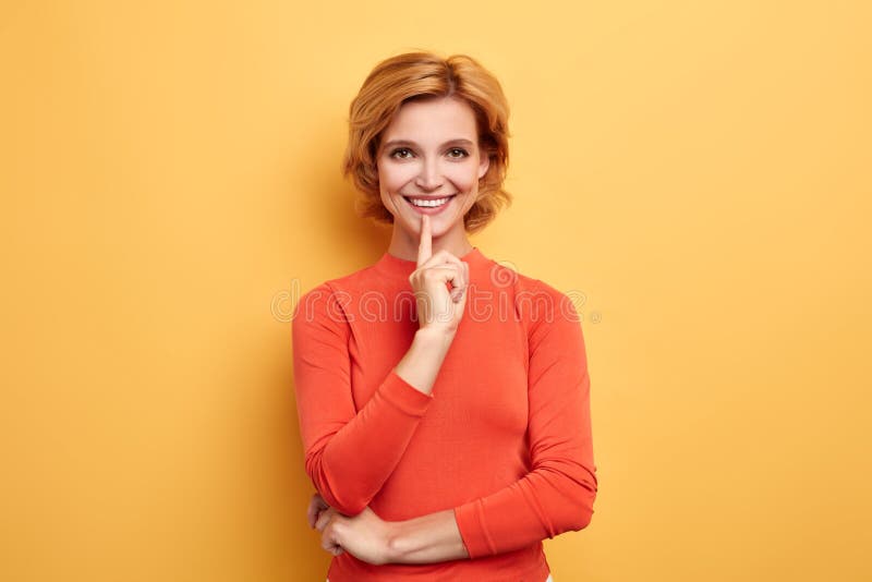 La giovane bella ragazza allegra che sogna di nuovo vestito, tiene il dito sulle labbra immagine stock libera da diritti La giovane bella ragazza allegra che sogna di nuovo vestito, tiene il dito sulle labbra immagine stock libera da diritti