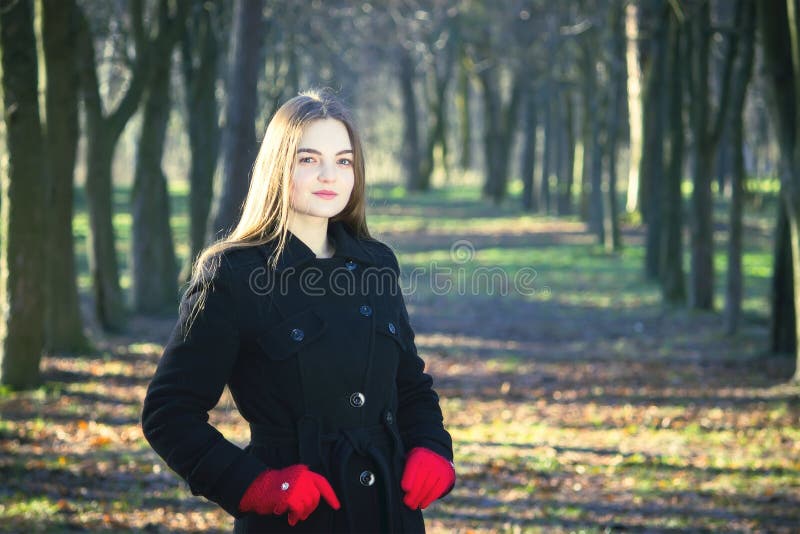 La giovane bella ragazza nei guanti rossi di un cappotto nero che esplora il fumo della foresta della molla parcheggia fotografia stock La giovane bella ragazza nei guanti rossi di un cappotto nero che esplora il fumo della foresta della molla parcheggia fotografia stock