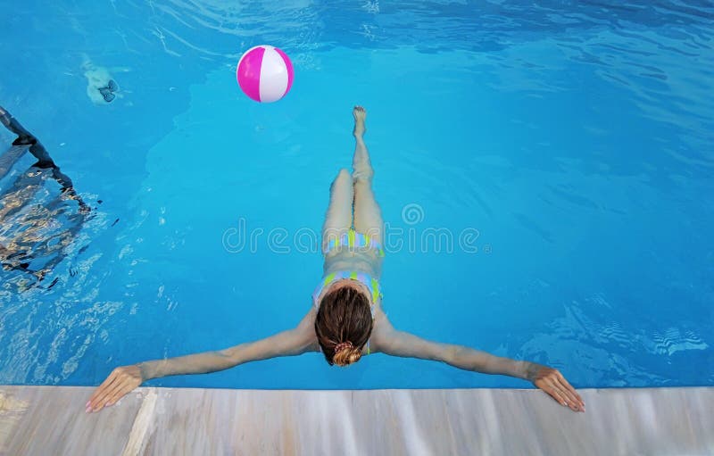 La giovane bella ragazza è rilassantesi e nuotante nella piscina blu con una palla rosa dentro la fine su fotografia stock La giovane bella ragazza è rilassantesi e nuotante nella piscina blu con una palla rosa dentro la fine su fotografia stock